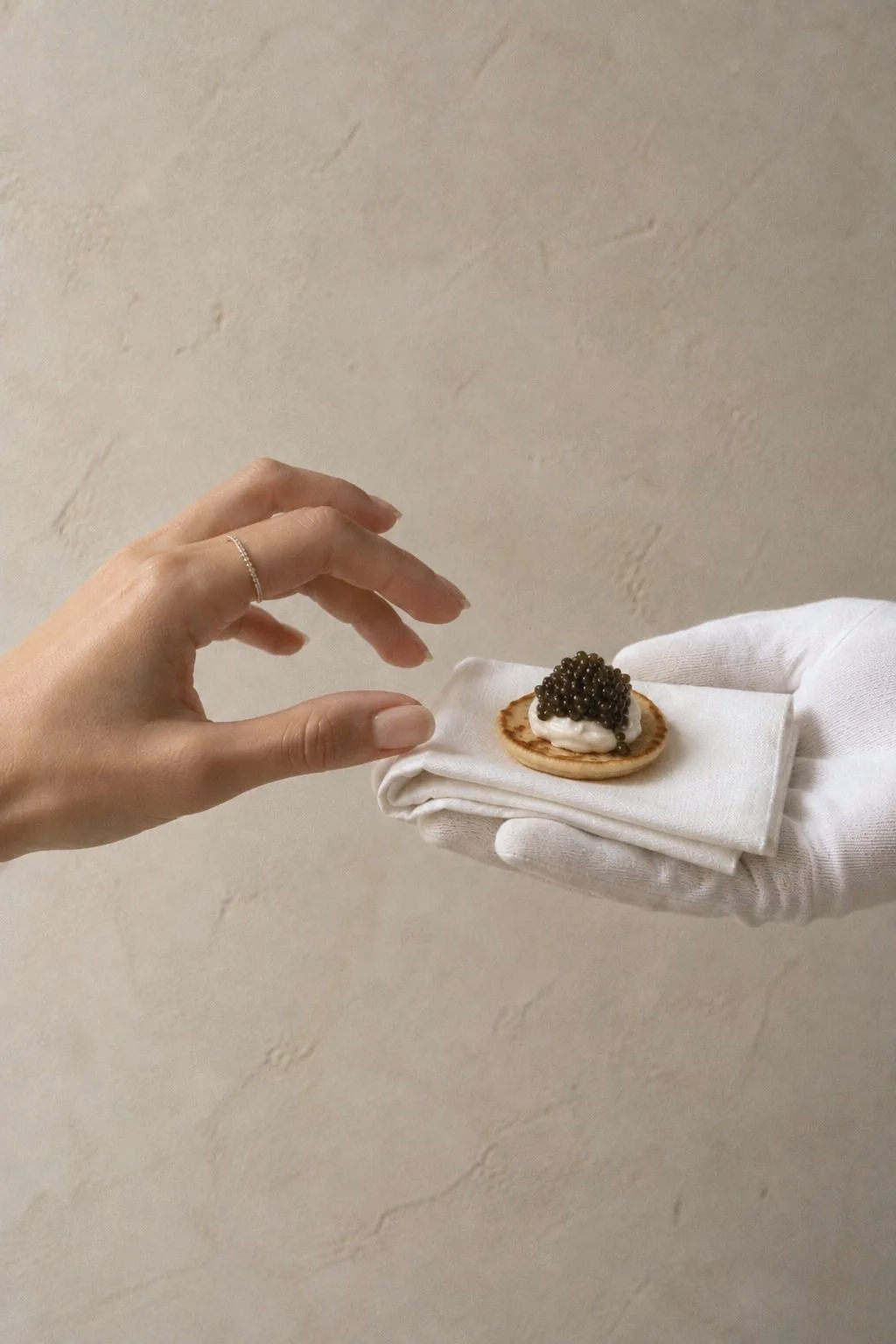Ein Blini mit Kaviar wird von einer behandschuhten Hand auf einer Serviette gereicht