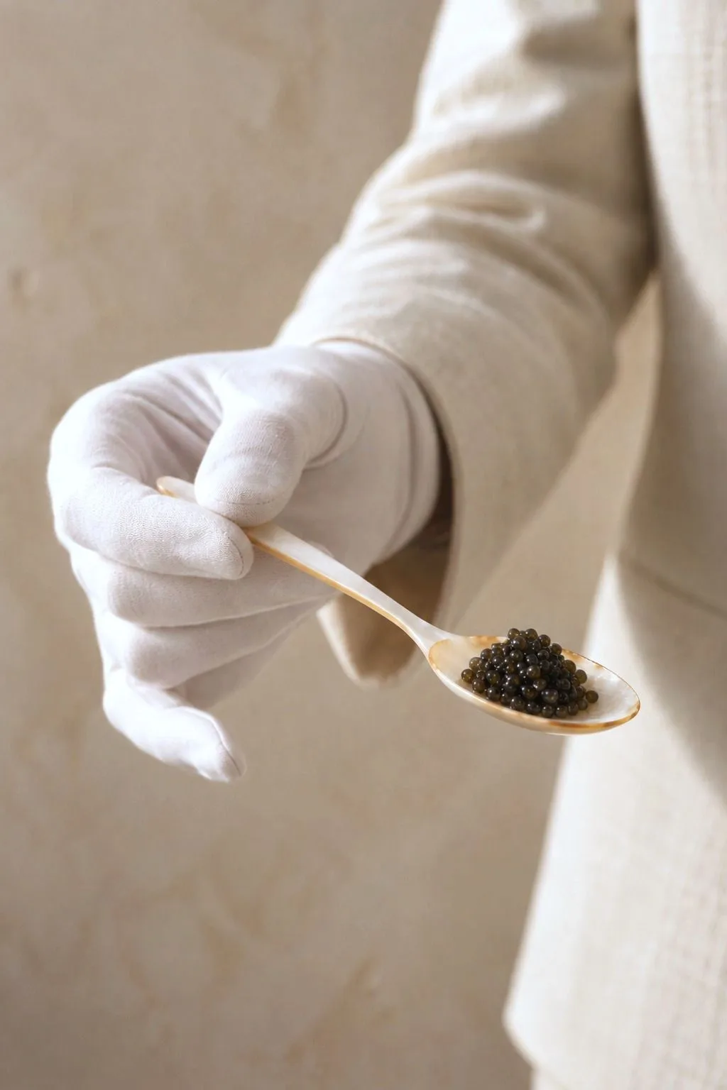 Maître de service ganté de blanc présentant une cuillère de nacre garnie de caviar